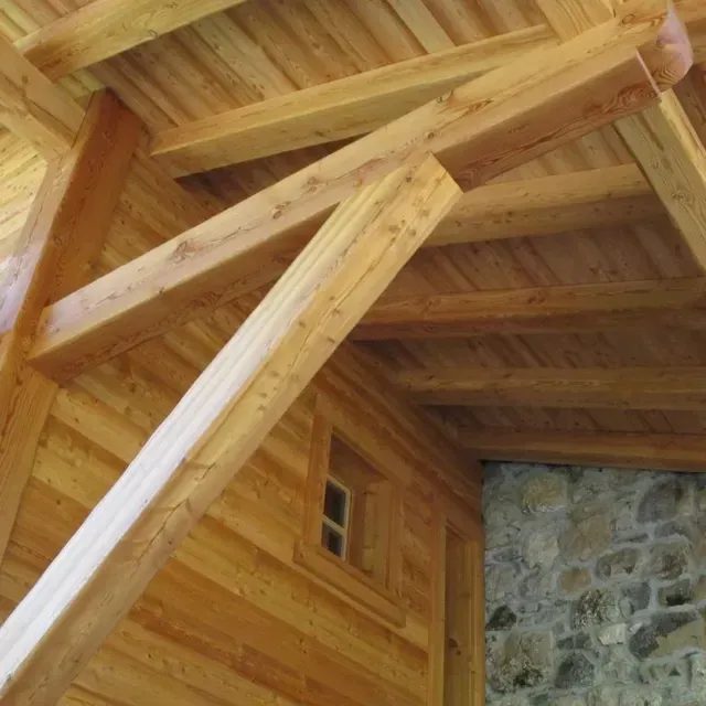 Charpente de toit en bois avec poutres apparentes et mur en pierre à l'intérieur d'un bâtiment rustique.