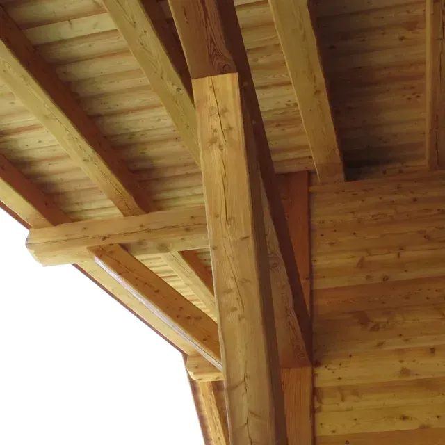 Poutres de toit en bois et un poteau de soutien sous une structure extérieure couverte.
