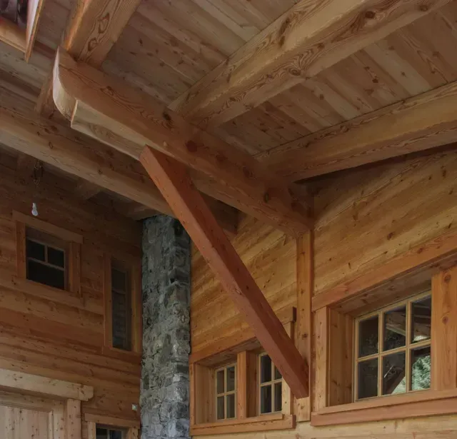 Plafond de véranda en bois avec poutres apparentes et fenêtres à côté d'une cheminée en pierre