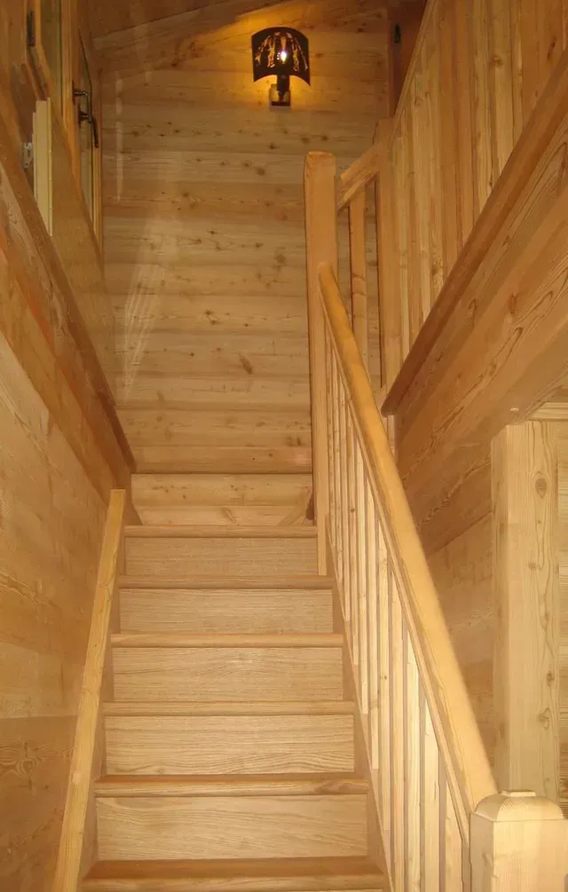 Escalier en bois dans un intérieur étroit lambrissé, avec une suspension lumineuse en haut.