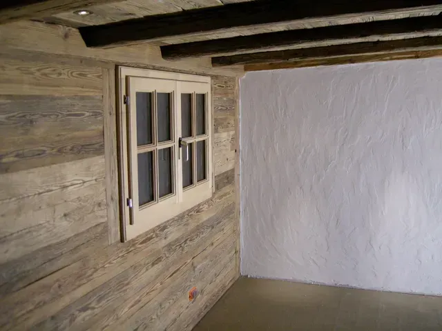 Coin de pièce rustique avec mur en bois, petite fenêtre et mur en plâtre blanc.