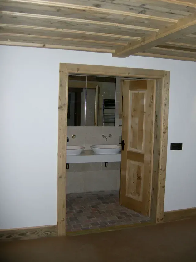 Porte en bois donnant sur une petite salle de bains avec lavabo et miroir.