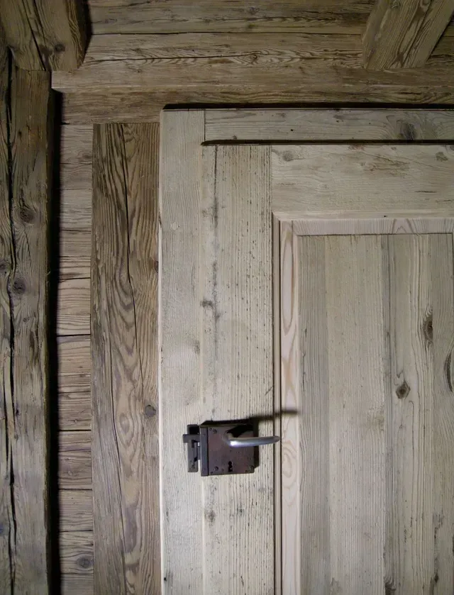 Gros plan sur une porte rustique en bois avec un loquet en métal foncé et un grain de bois patiné.