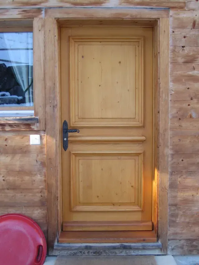 Porte extérieure en bois avec poignée noire sur le mur d'une cabane en rondins, à côté d'une fenêtre