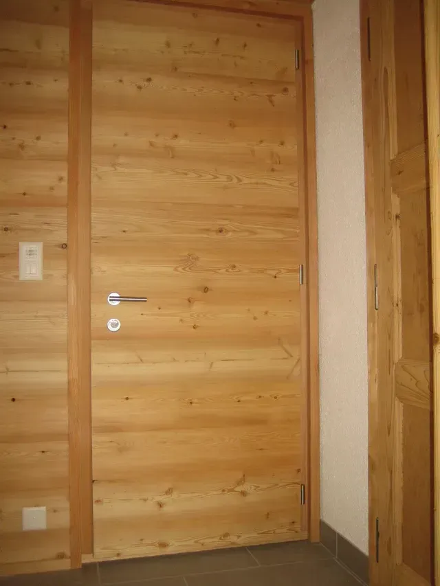 Porte intérieure en bois avec poignée argentée dans une pièce lambrissée de pin