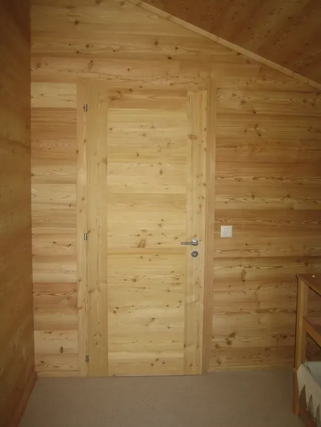 Mur de chambre lambrissé avec une porte en bois clair et un petit cadre de lit sur la droite.