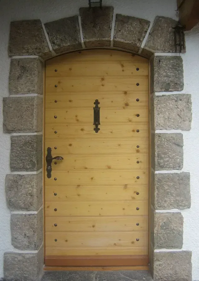 Porte cintrée en bois encadrée de blocs de pierre brute, avec des ferrures en fer noir.