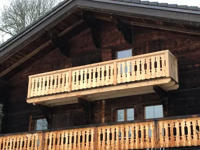 Chalet en bois avec deux balcons couleur crème se détachant sur un ciel nuageux