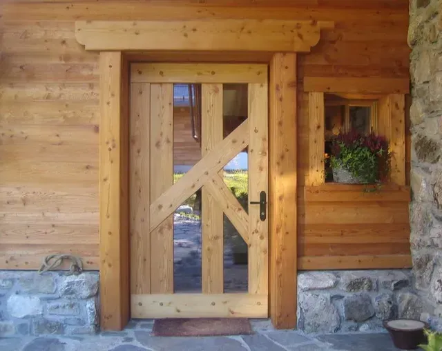 Porte d'entrée rustique en bois avec une porte vitrée et en bois, un socle en pierre et une jardinière sur la droite.