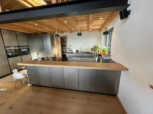 Cuisine moderne avec plafond en bois, armoires grises, grand îlot et coin repas ouvert.