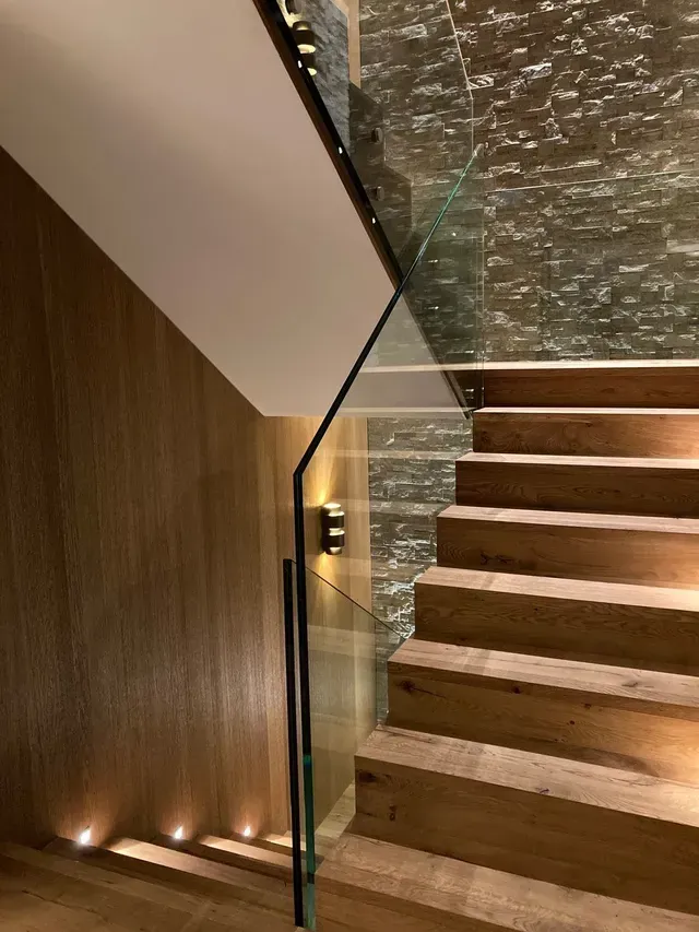 Escalier moderne en bois avec rampe en verre et éclairage mural chaleureux dans un intérieur élégant