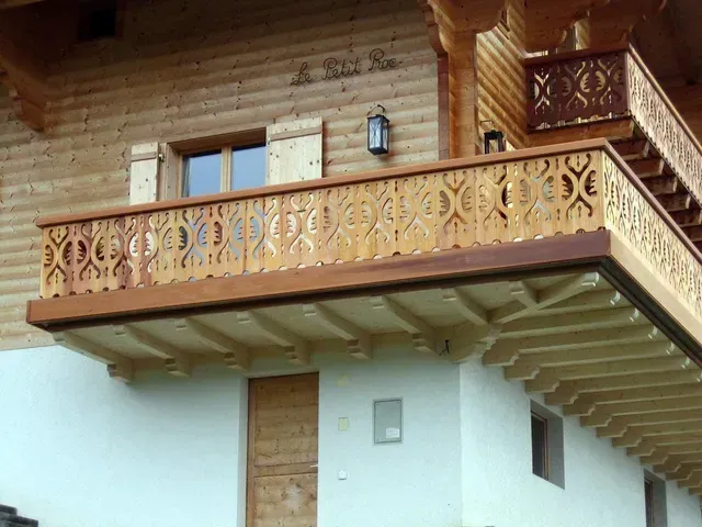 Maison de style chalet en bois avec balcon sculpté et mur inférieur blanc sous un toit en surplomb