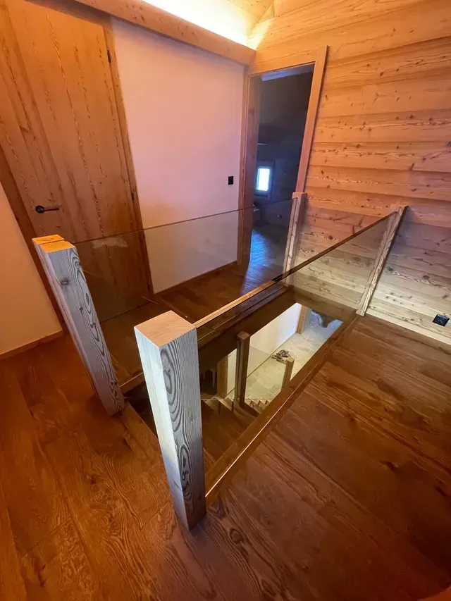 Palier d'escalier lambrissé avec une rambarde en verre et une porte ouverte au-dessus.