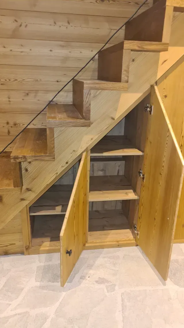 Placards de rangement en bois sous l'escalier avec portes ouvertes dans une pièce rustique