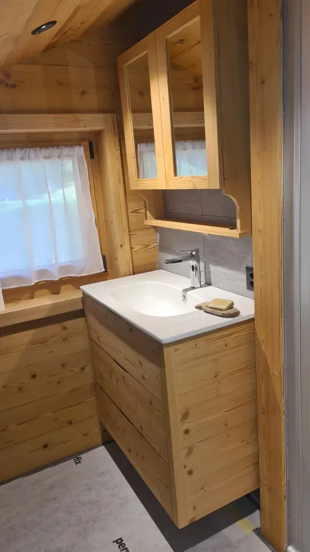Salle de bains lambrissée avec meuble-lavabo, armoire à miroir et fenêtre à rideaux