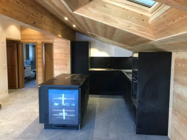 Cuisine moderne vide avec des armoires noires, un îlot central et un plafond incliné en lambris.