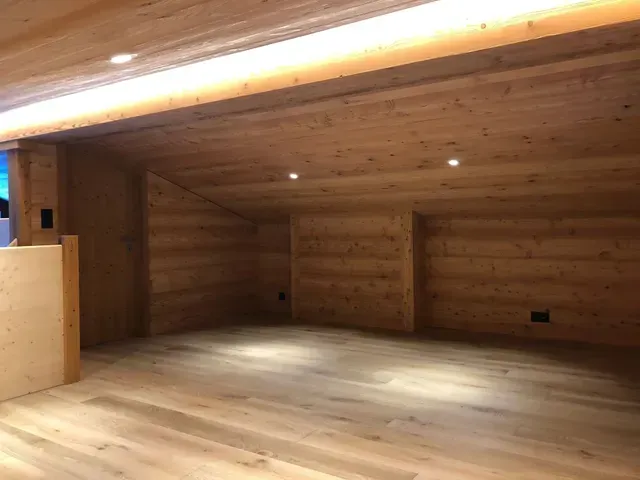 Pièce intérieure en bois avec plafond mansardé, éclairage encastré et parquet clair.