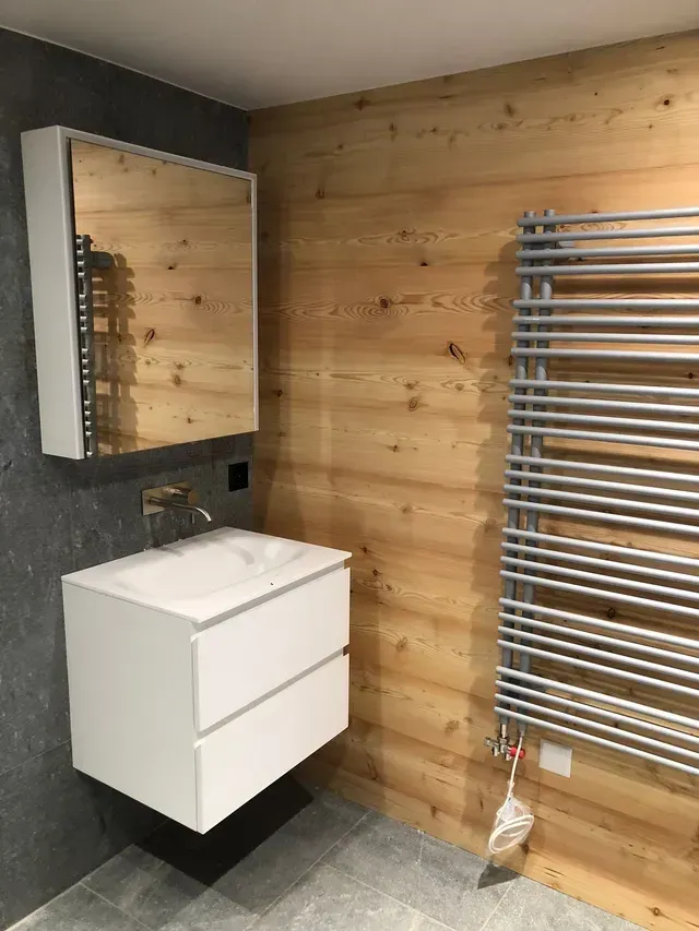 Salle de bains moderne avec meuble-lavabo blanc, armoire à miroir et sèche-serviettes chromés sur un mur lambrissé.