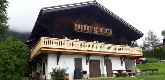 Chalet alpin en bois avec balcons sur un flanc de colline verdoyant sous un ciel nuageux