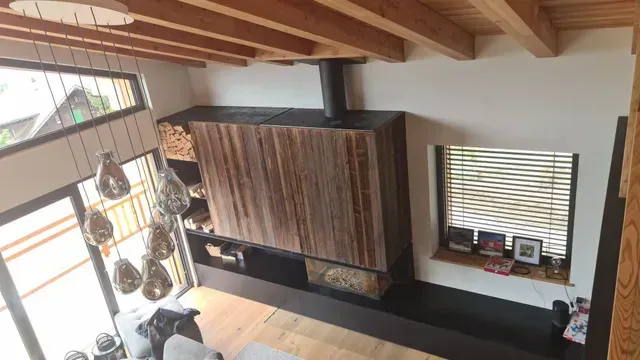Salon moderne avec cheminée lambrissée, poutres apparentes, grandes fenêtres et plantes suspendues