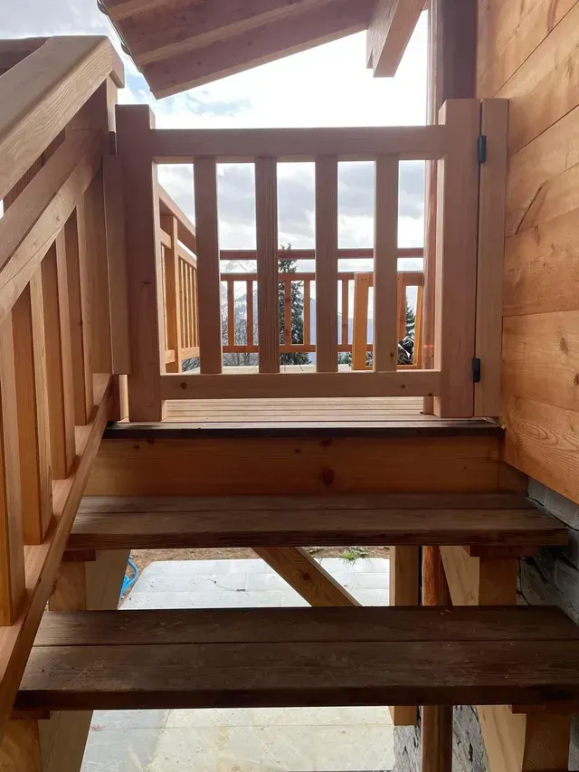 Escalier en bois à l'intérieur d'une structure en bois, menant à une balustrade offrant une vue sur l'extérieur.
