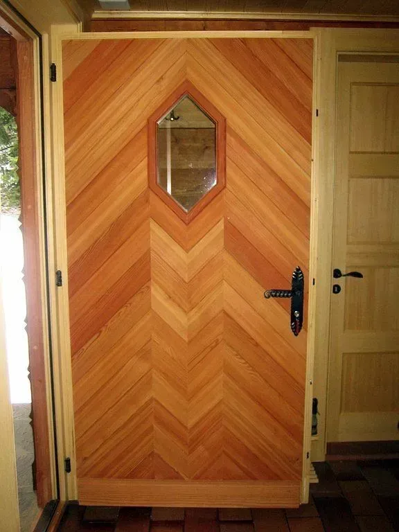 Porte d'entrée à panneaux de bois avec une petite fenêtre hexagonale et une poignée noire dans un couloir