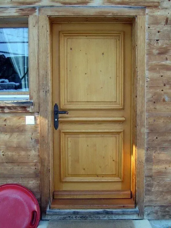 Porte d'entrée en bois encastrée dans un mur rustique en rondinté