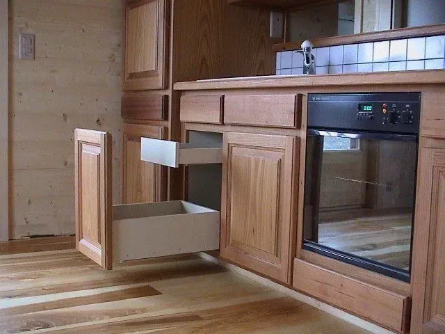 Cuisine en bois avec tiroirs ouverts, évier et four encastré, le tout sur un sol en parquet.