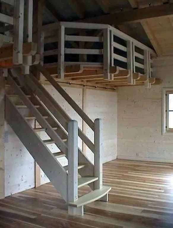 Loft intérieur avec escalier en bois menant à une petite mezzanine dans une pièce ressemblant à une cabane