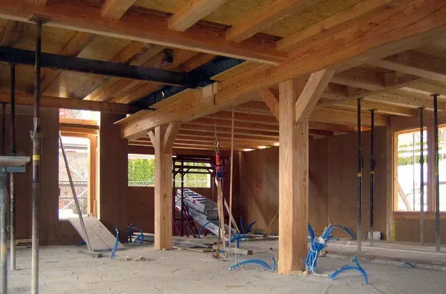Intérieur d'une maison inachevée avec poutres apparentes, fils électriques pendants et outils de construction au sol