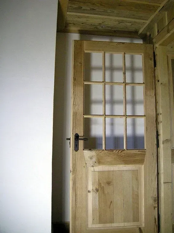 Porte intérieure en bois avec vitres et poignée noire dans un couloir rustique