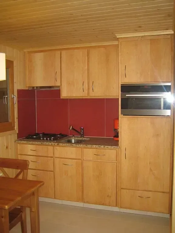 Petite cuisine en bois avec crédence rouge, placards clairs, évier et four encastré.