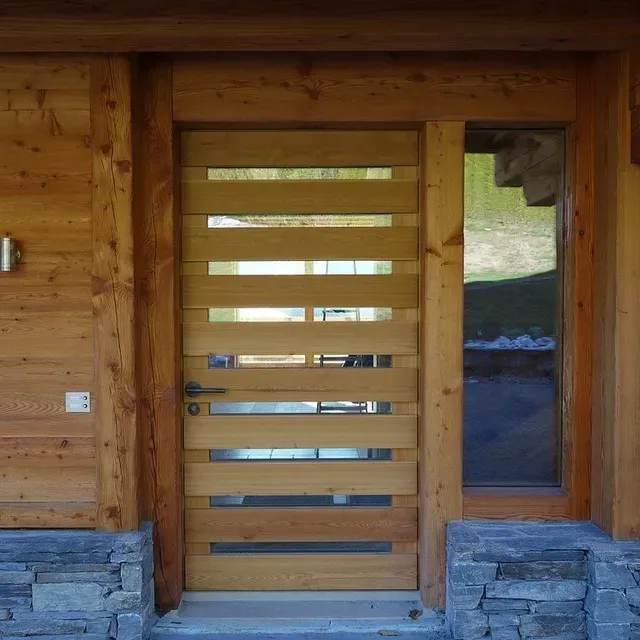 Porte d'entrée en bois à lattes horizontales sur un extérieur de cabane en rondins et plinthe en pierre