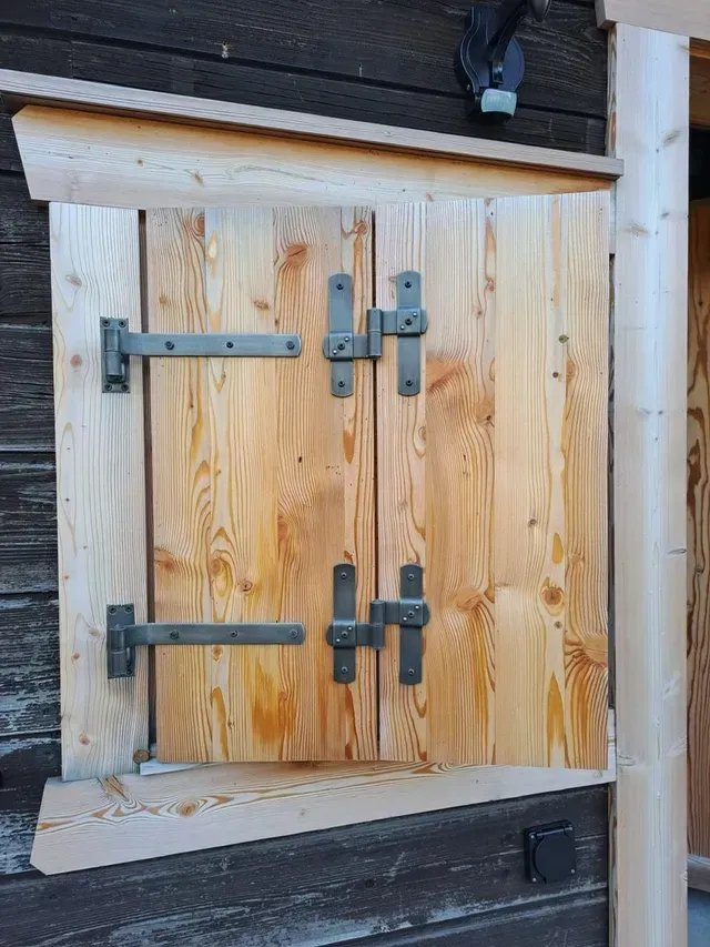 Porte de grange double en bois avec charnières et loquets en métal foncé sur un mur extérieur patiné par les intempéries