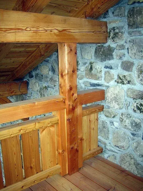 Poutres et rambarde en bois dans un coin de grenier rustique, à côté d'un mur en pierre.