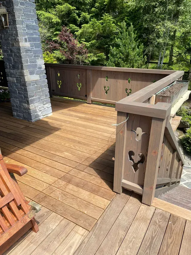 Terrasse en bois avec rambarde marron et pilier en pierre donnant sur un jardin luxuriant