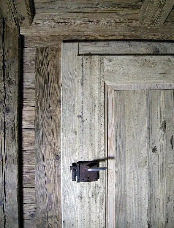 Gros plan sur une porte rustique en bois avec un loquet foncé et des planches patinées par le temps.