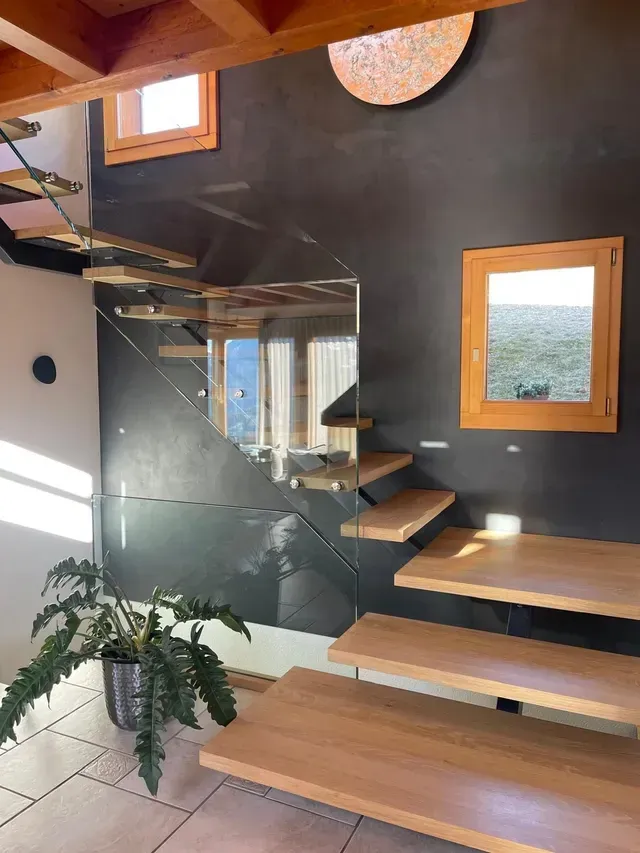 Escalier moderne avec rampe en verre, marches en bois et petites fenêtres dans un intérieur minimaliste