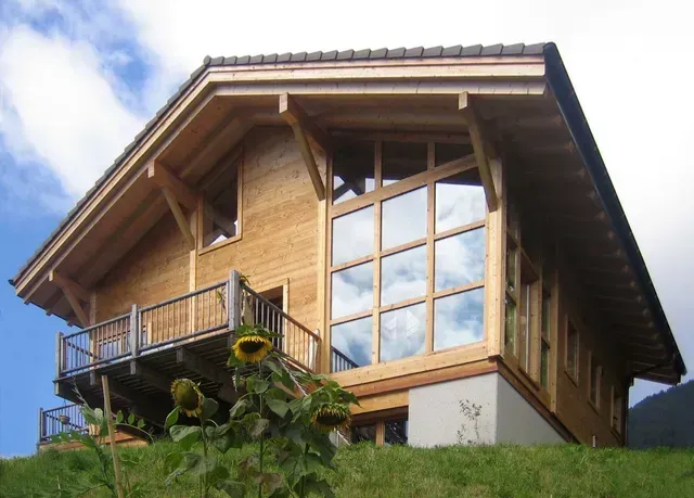 Maison en bois avec de grandes fenêtres et un balcon sur une colline herbeuse sous un ciel bleu