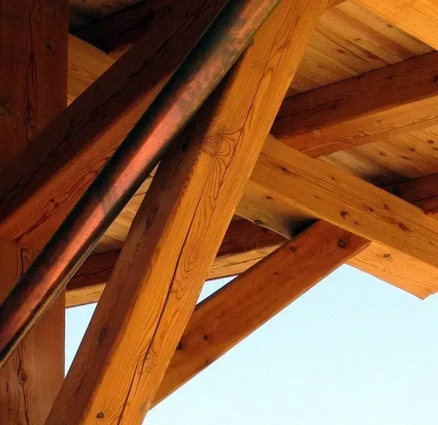 Poutres et contrefiches en bois se détachant sur un ciel bleu.