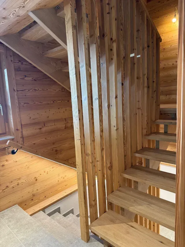 Escalier en bois et cloison à lattes verticales dans un intérieur chaleureux aux tons clairs