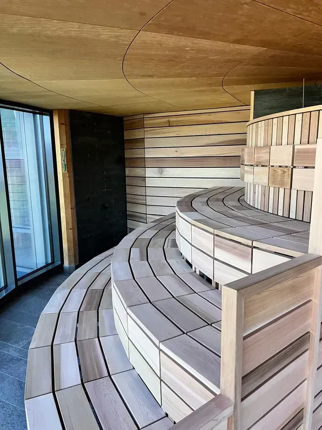 Bancs de sauna en bois courbé avec assises carrelées et une grande fenêtre sur la gauche