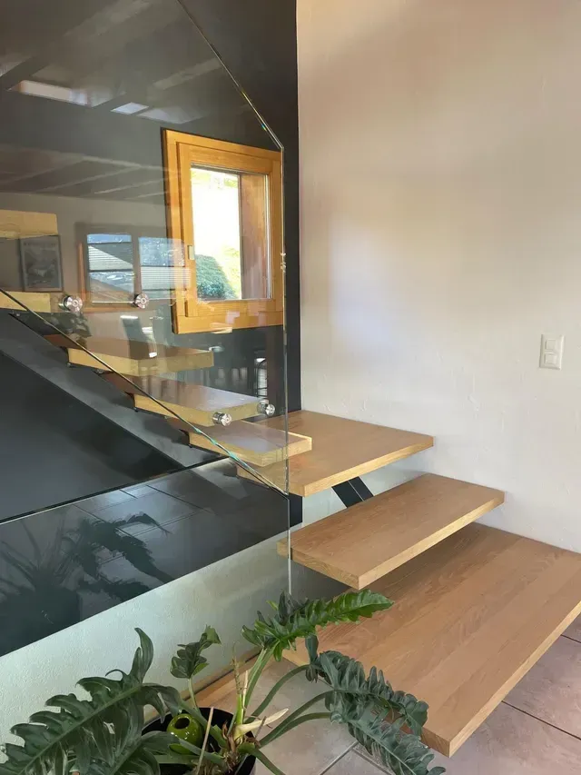 Escalier de bureau moderne avec marches en bois, rampe en verre et miroir mural près d'un mur blanc