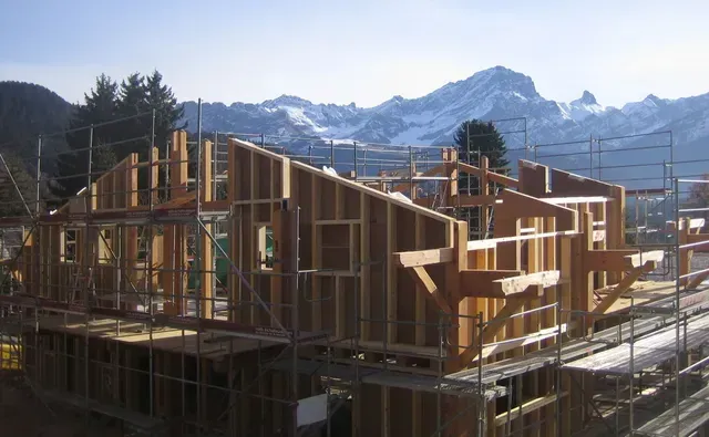 Bâtiment à ossature bois en construction, avec des montagnes en arrière-plan.