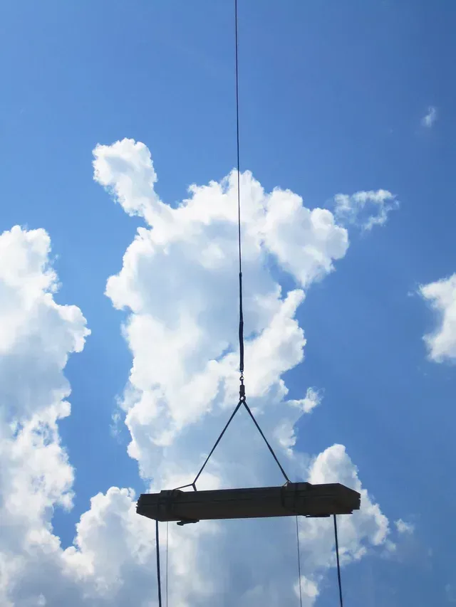 Poutre noire suspendue par des câbles se détachant sur un ciel bleu clair parsemé de nuages.