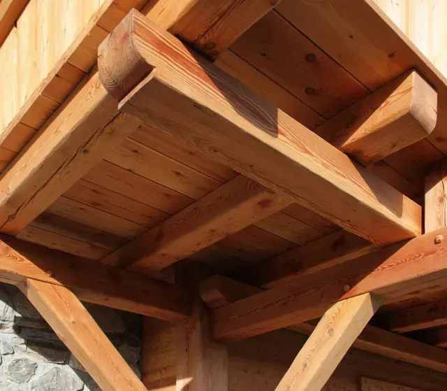 Gros plan sur des poutres et des supports en bois sous un toit, illustrant une construction rustique en bois.