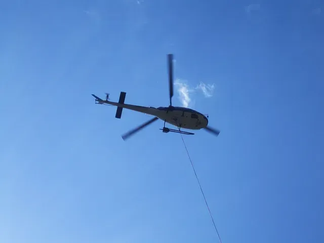 Un hélicoptère se détachant sur un ciel bleu remorquait un long câble en dessous.
