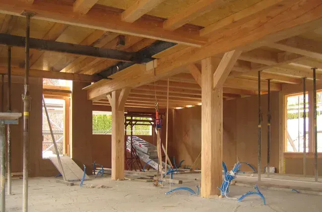 Intérieur d'une maison en bois en construction, avec poutres apparentes, charpente et outils au sol.
