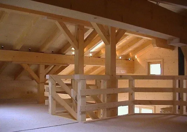 Intérieur d'un grenier en bois avec poutres apparentes, balustrades et petites fenêtres, baigné d'une douce lumière du soleil