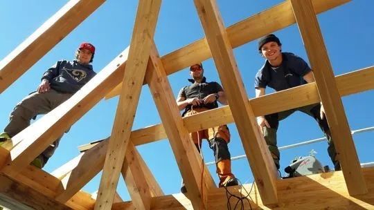 Des ouvriers debout sur une charpente de toit en bois sous un ciel bleu clair